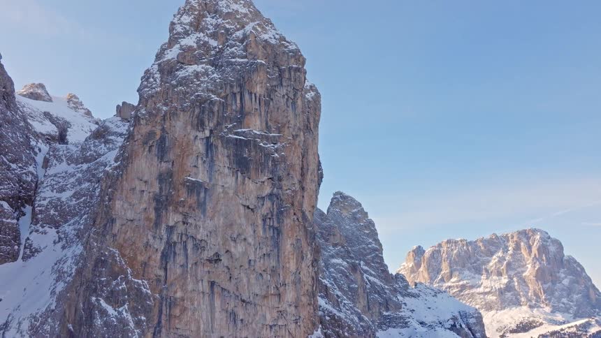 A slow aerial pullback reveals the stunning, snow-covered peaks of the Sella Towers in the Italian Dolomites on a sunny day
