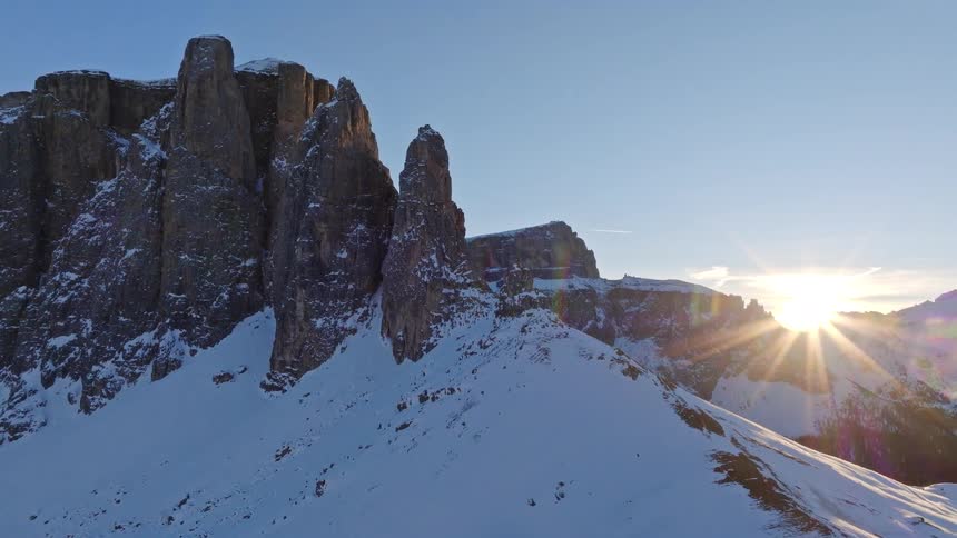 A majestic aerial view of the sun rising behind the rugged, snow-covered peaks of the Dolomites