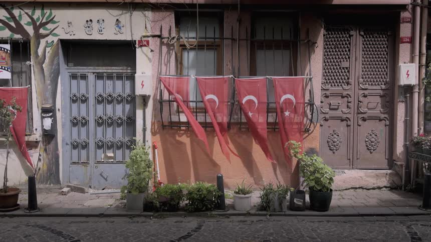 Turkish flags hang from the facade of an old rustic building and blow gently in the wind on a cobblestone city street