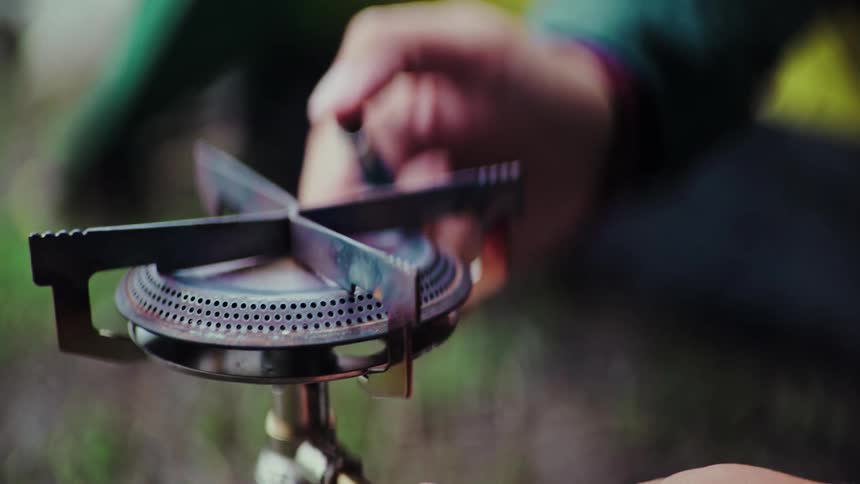 A person lights a portable gas camping stove with a spark in an extreme close-up slow motion shot