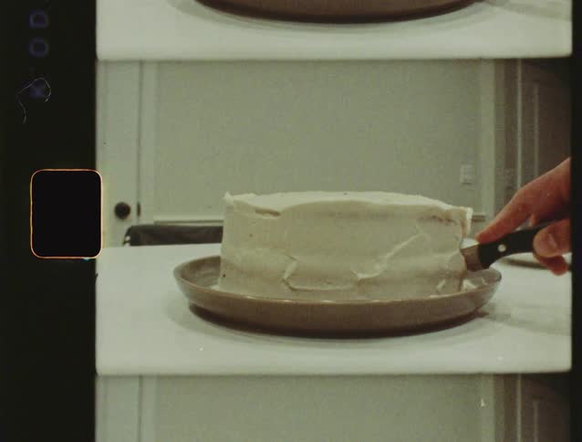 Vintage film footage shows a person cutting into a celebratory white frosted cake