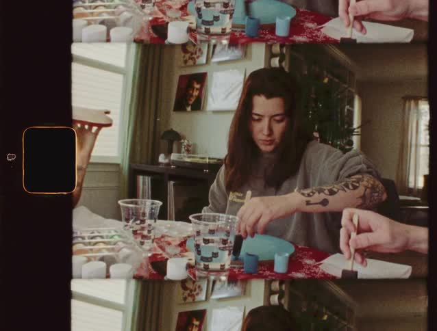 Vintage 8mm film footage shows a tattooed couple painting holiday crafts at a table decorated for Christmas