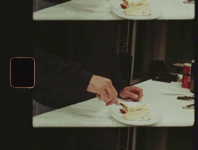 A man with a beard smiles and eats a slice of cake in a warm kitchen, captured with a nostalgic film aesthetic