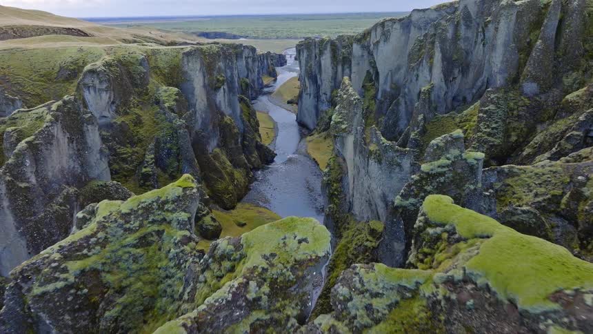 A majestic aerial flight through the dramatic, moss-covered Fjadrargljufur Canyon in southern Iceland, following the winding river below