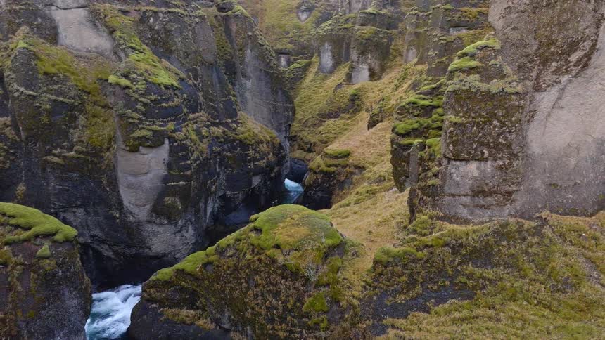 An aerial shot pans slowly across the majestic, moss-covered rock formations of a deep canyon with a turquoise river flowing below