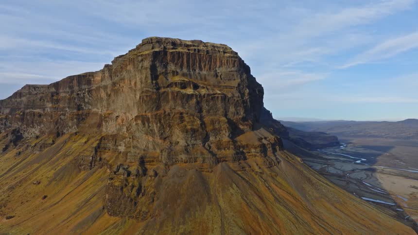 Epic aerial pullback reveals a majestic mesa-like mountain standing solitary in the vast, rugged highlands of Iceland