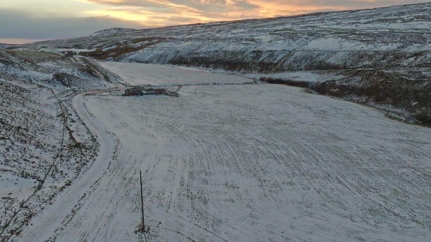 An aerial view of a person walking on a snow-covered road in a vast winter landscape as the camera pans up to a beautiful sunrise