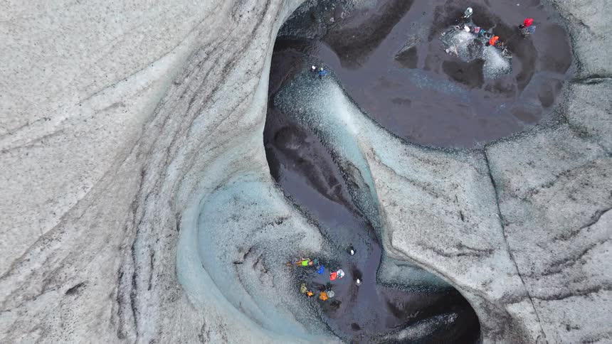 An epic aerial reveal shows a group of adventurers exploring and swimming in a vast, winding glacial ice canyon