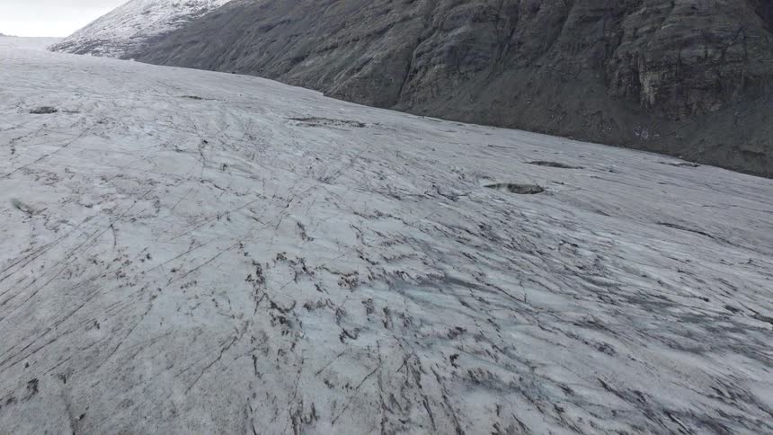 Aerial drone shot pulls back from a moulin and crevasses on a vast glacier revealing a majestic snow-capped mountain