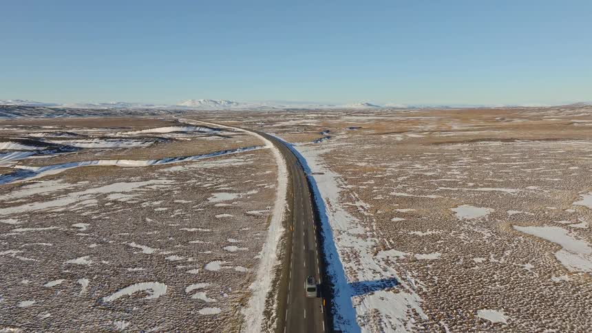 Aerial shot follows a camper van on a solo road trip through a vast, snowy landscape in Iceland as the camera slowly pulls back to reveal the remote scenery