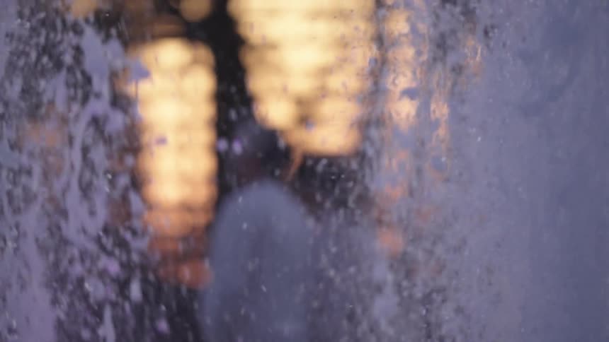 Mesmerizing abstract shot of water flowing over a glass surface, distorting the warm, glowing bokeh lights in the background