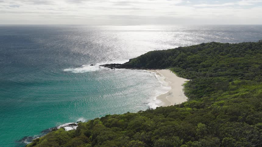 A beautiful aerial shot of a pristine, secluded beach cove with turquoise water and lush green forest