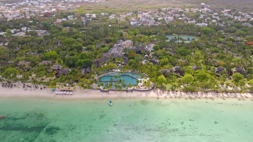 A stunning aerial shot pulls back to reveal a luxurious tropical resort with a beautiful pool on the white sandy coast of an island