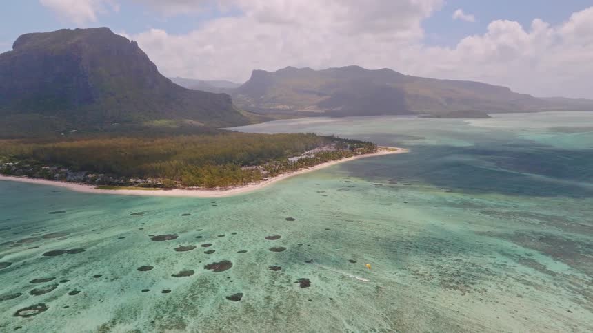 A stunning aerial panorama showcases the Le Morne peninsula in Mauritius, surrounded by a vibrant turquoise lagoon and distant mountains