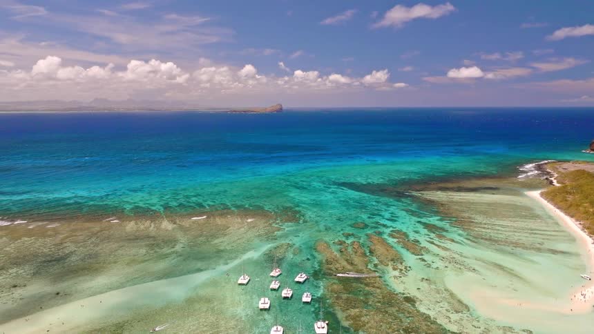 Stunning aerial pullback view of catamarans anchored in a vibrant turquoise lagoon off a tropical island coast