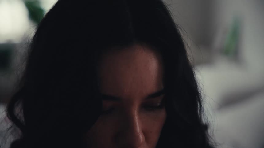 An intimate close-up of a woman's face shows her looking down with a somber and pensive expression