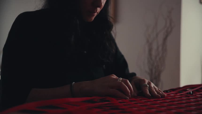 A close up on an artisan's hands as she meticulously weaves red straps into a patterned design