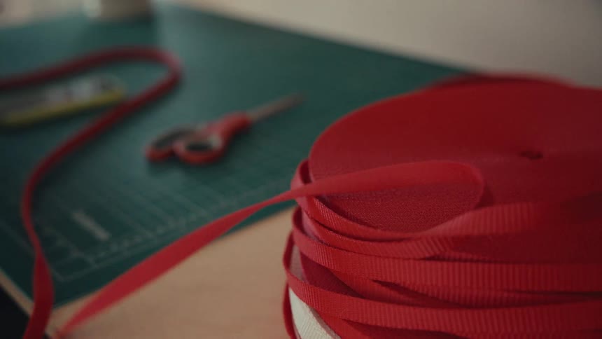 A close-up of a person's hands unspooling a length of red ribbon from a large roll on a workbench