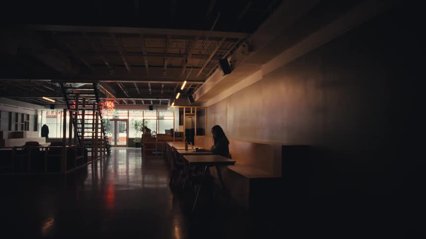 A solitary figure is illuminated by a single light while working late in a vast, empty modern space