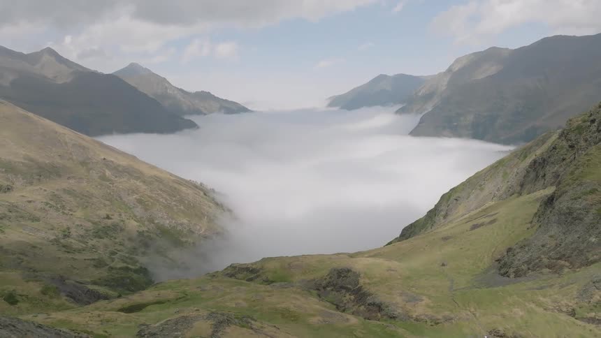 A breathtaking aerial shot pulls back to reveal a vast mountain valley filled with a sea of clouds
