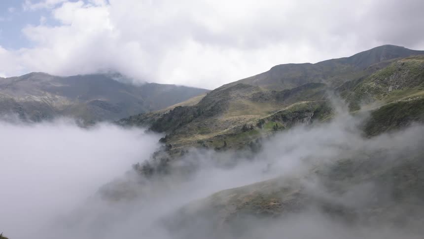 A stunning view of a mountain valley with a thick layer of fog rolling across the landscape on an overcast day