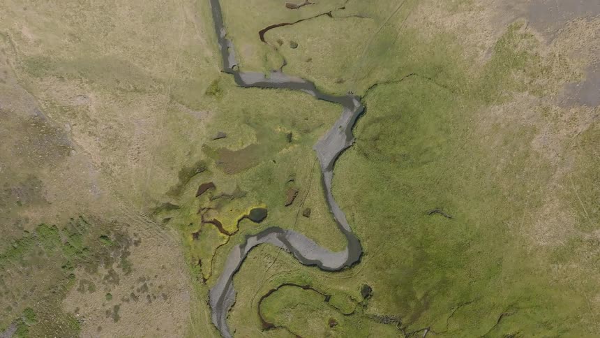 A static, top-down aerial view shows a small, meandering river carving its path through a green and earthy landscape