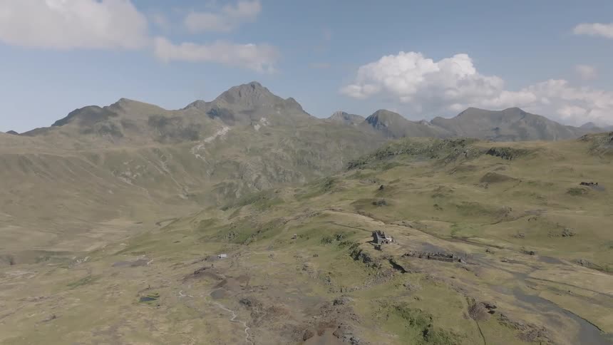 An epic aerial view slowly reveals a vast, rugged mountain valley under a blue sky with clouds