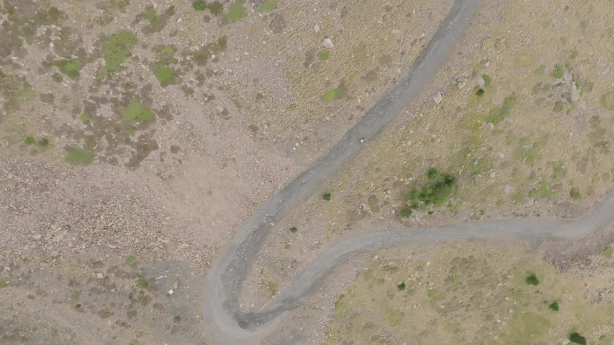Top-down aerial view of a lone hiker walking along a winding dirt path in a rugged, mountainous landscape