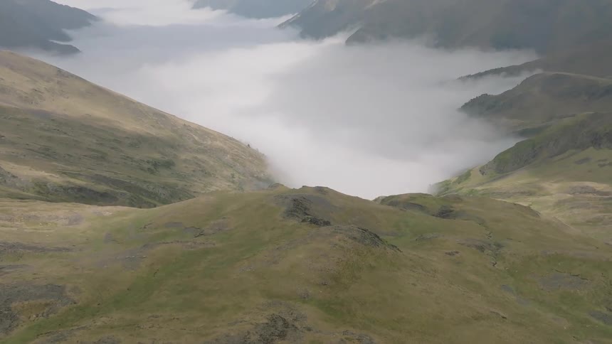 A majestic aerial view pushes forward from a rugged mountaintop to reveal a serene sea of clouds filling the valley below