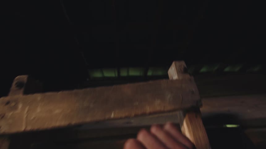 A first-person perspective of climbing a rustic wooden ladder into the dark, shadowy loft of an old barn