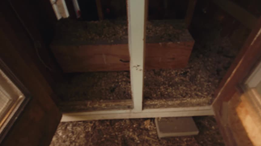 A first-person point of view shot of hands opening the doors to a dark and rustic wooden chicken coop
