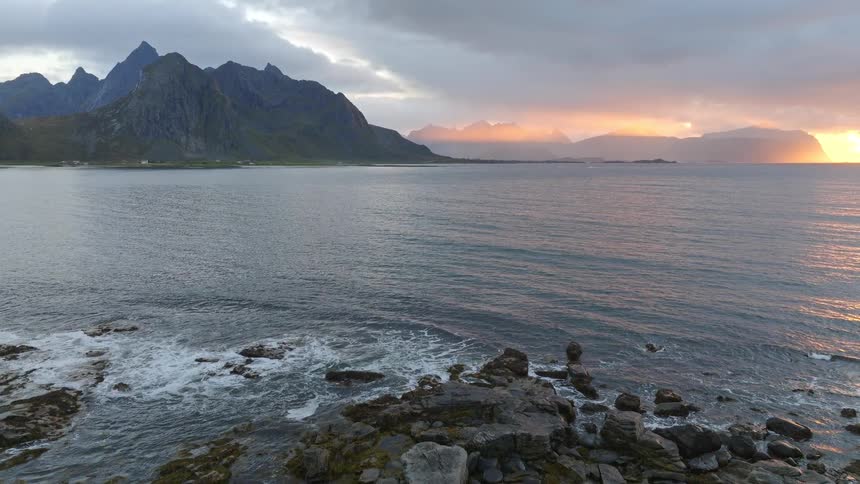 A dramatic sunset casts its final golden rays over a tranquil fjord surrounded by majestic mountains and a rugged, rocky coastline