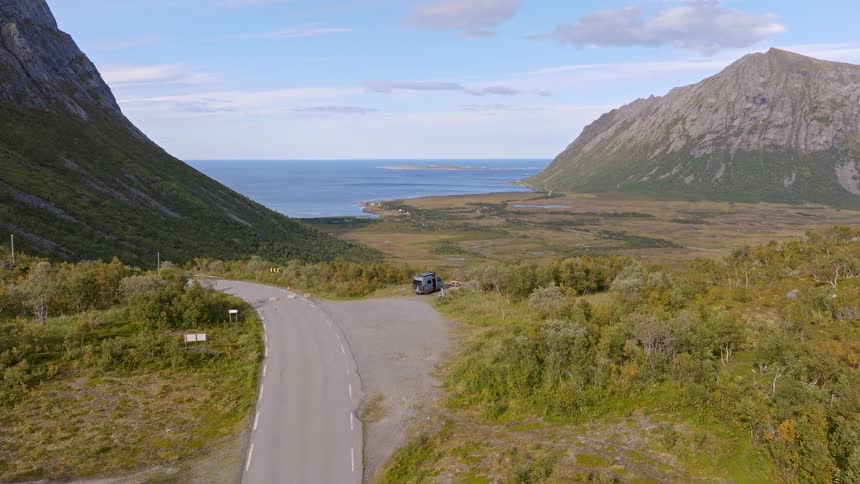 Aerial view pulls back to reveal a man and his dog enjoying the epic scenery of a mountain valley from their campsite next to their adventure van