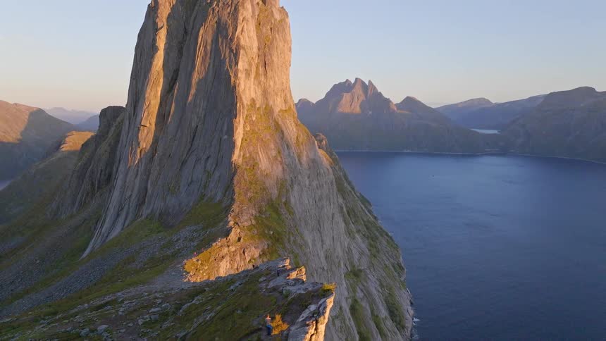 Breathtaking aerial view reveals hikers on the narrow ridge of Segla mountain, overlooking a vast Norwegian fjord during a golden sunset