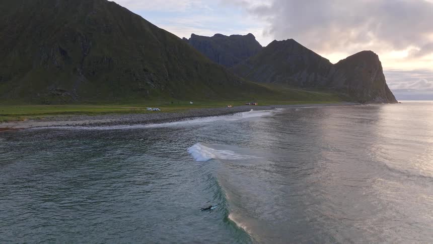 Aerial shot of surfers enjoying the evening waves along a majestic and rugged Nordic coastline