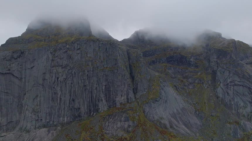 An epic aerial view of a craggy mountain peak disappearing into a thick layer of fog on an overcast day
