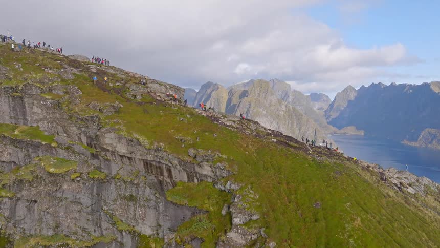 Stunning aerial shot follows hikers on a mountain ridge, revealing a breathtaking view of a Norwegian fjord and fishing village