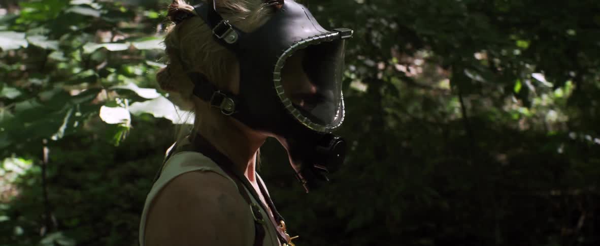 A woman wearing a gas mask looks around a forest