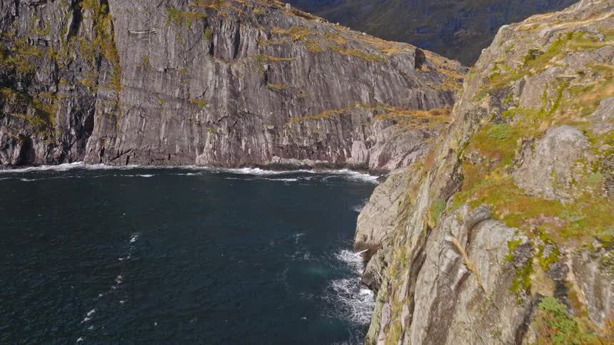 An epic aerial pullback reveals a stunning, rugged coastline with steep cliffs and snow-capped mountains meeting the ocean