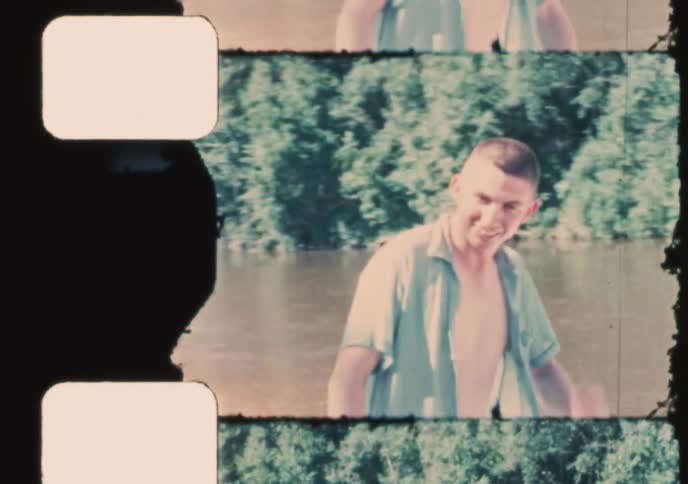 Vintage 1960s home movie footage shows people in swimwear enjoying a sunny day at a sandy river beach
