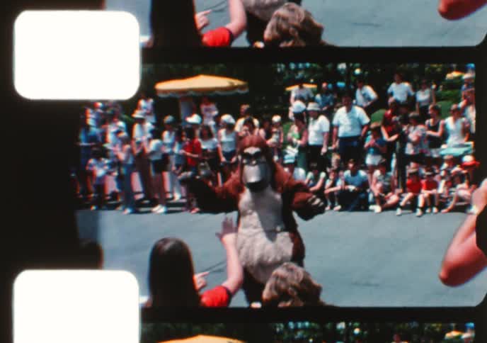 Nostalgic 1970s home movie footage shows a vibrant character parade with marching bands at a Disney theme park