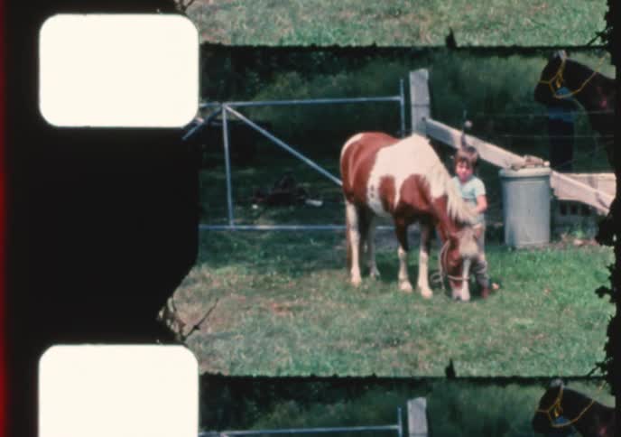 Vintage home movie captures a young boy proudly standing next to his pet pony grazing in a grassy field