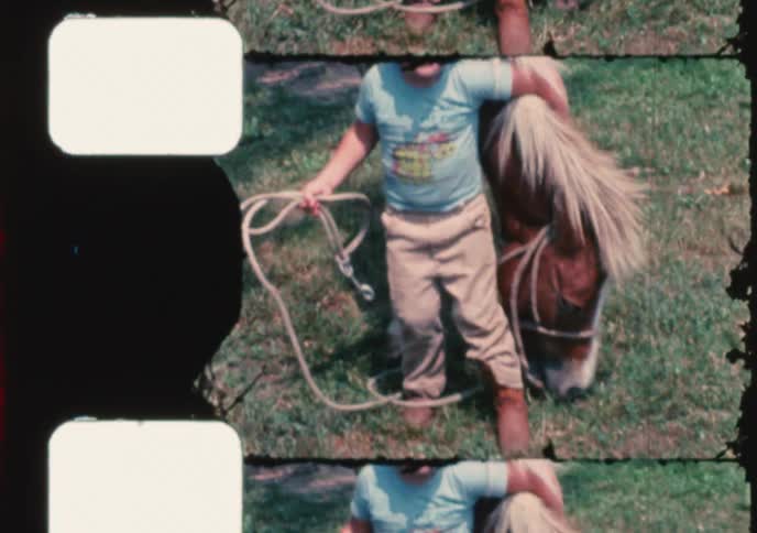 Vintage 8mm footage shows a cute little boy smiling happily while posing next to a pony in a grassy field