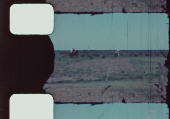 Vintage 8mm film captures a distant view of cowboys riding on horseback across a vast, open prairie