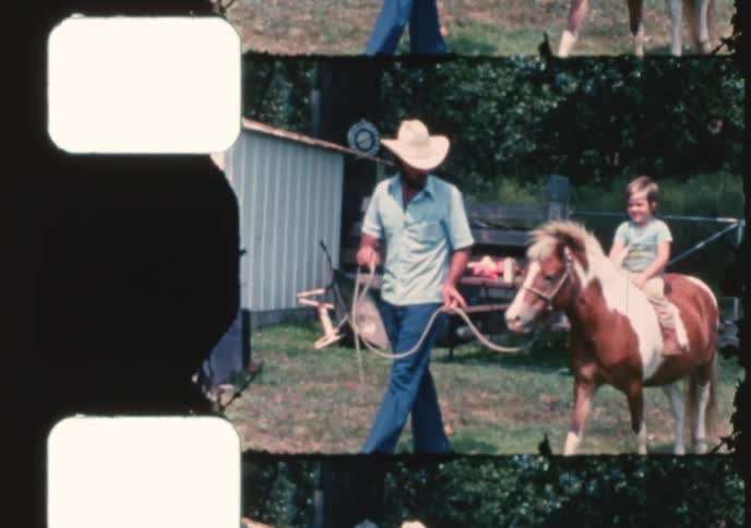 A father in a cowboy hat leads his smiling child on a pony ride in this vintage 8mm film clip