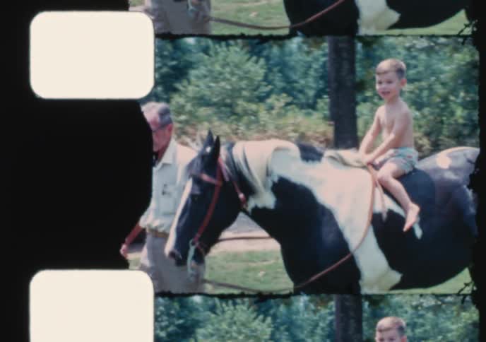 A vintage home movie shows a happy little boy riding a pinto pony led by his grandfather on a sunny summer day