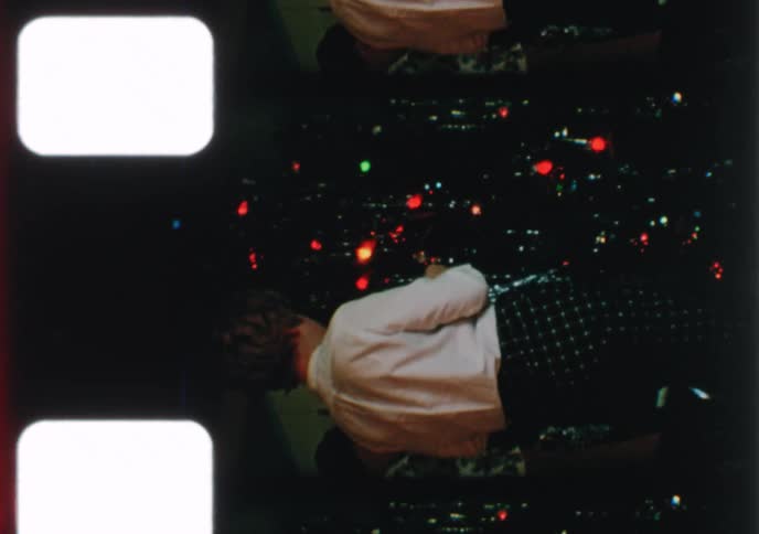 Vintage 8mm home movie captures a family decorating their Christmas tree with colorful lights and tinsel