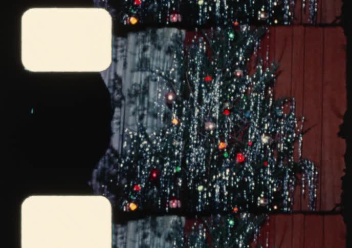 A vintage 8mm home movie captures a nostalgic Christmas tree covered in shiny tinsel with presents underneath