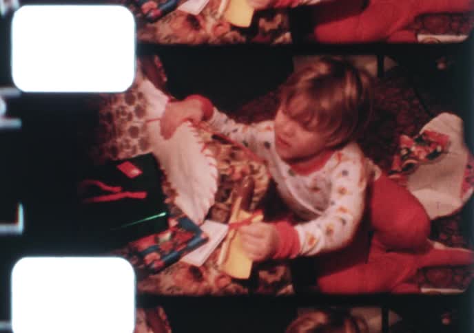 A vintage 16mm film captures a young child opening presents on Christmas morning and a family gathering together