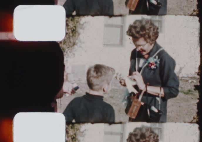 Vintage home movie footage shows a woman and a young boy interacting at a family gathering in the 1950s